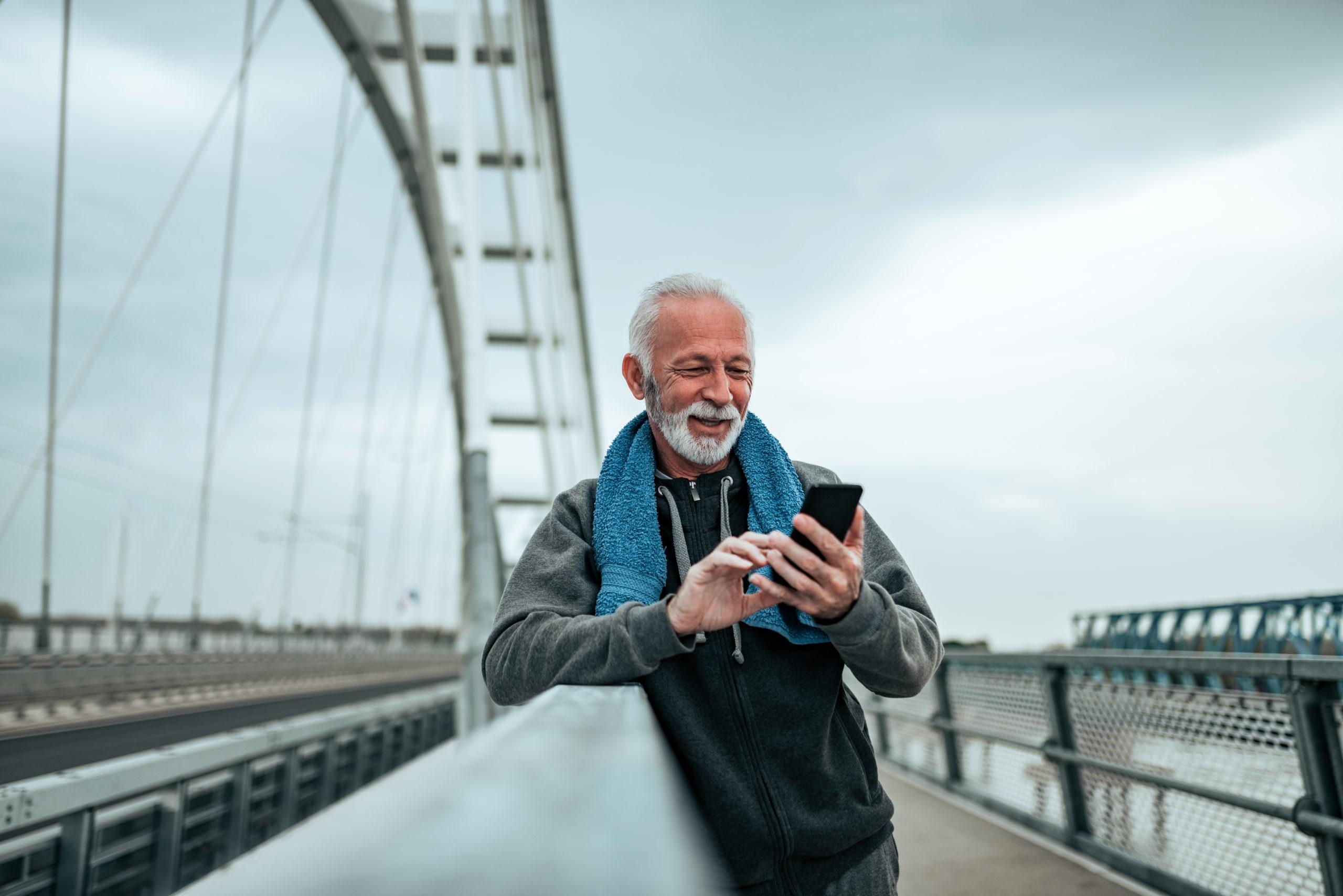 Active senior man using mobile phone after a run or workout outdoors
